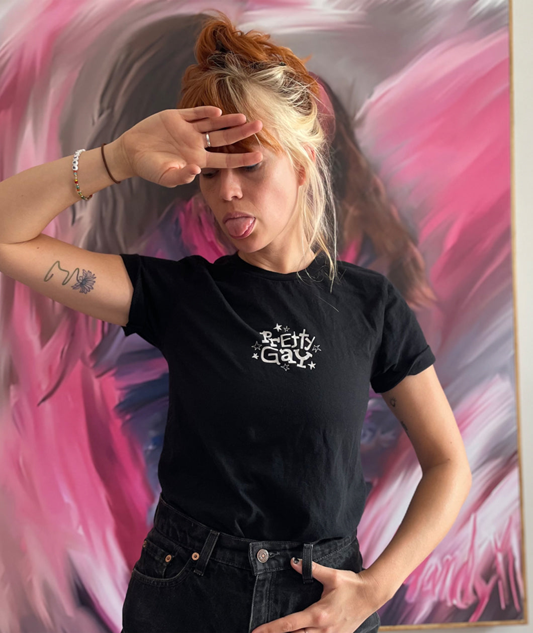 A photo of Catherine McCafferty posing, wearing a black t-shirt. The shirt reads "Pretty Gay" and has little star illustrations around it. From Pretty Gay.