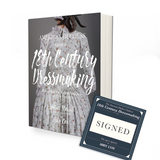 A book with a charcoal gray background and the image of a lady wearing a white bodices dress with a small pink flower pattern appearing to be from the 18th century. The title of the book says The American Duchess Guide to 18th Century Dressmaking. There is a square dark blue bookplate next to the book that indicates it is signed by the author Abby Cox.