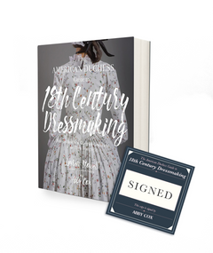A book with a charcoal gray background and the image of a lady wearing a white bodices dress with a small pink flower pattern appearing to be from the 18th century. The title of the book says The American Duchess Guide to 18th Century Dressmaking. There is a square dark blue bookplate next to the book that indicates it is signed by the author Abby Cox.