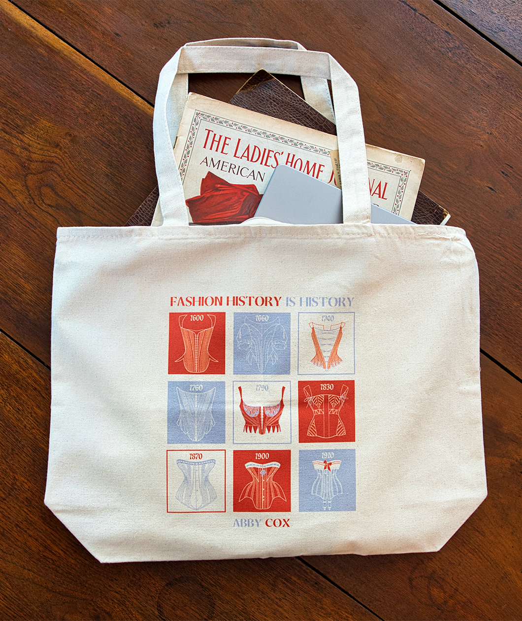 Canvas tote with red and light purple square design on the front. Text says FASHION HISTORY IS HISTORY and then under the design says ABBY COX.