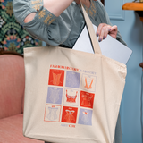 Woman in a blue dress holding a canvas tote with red and light purple square design on the front. Text says FASHION HISTORY IS HISTORY and then under the design says ABBY COX. She is placing a laptop into the bag which seems to take up about half of the space.