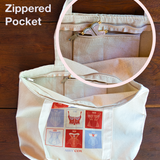 Upper left text says Interior Zippered Pocket and image shows a canvas tote with red and light purple square design on the front. There is a circular image on top that shows the top of the tote unzippered to reveal a smaller zippered pocket on the interior with a pink and gold corset pin sticking out.