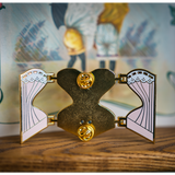 Back of the gold hard enamel pin when it is open and you can see either half of the outer corset on either side connected to the central back piece by four gold hinges. Two gold butterfly clasps are on the top and bottom of the back of the pin to secure it.