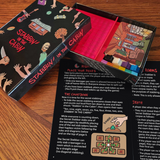 Stabbin in the Cabin Board game box and instructions booklet on a wooden table. Bo is open so you can see the 100 red translucent cubes, 10 meeples, and deck of cards. Outside of the box is a glossy black with the character printed on it and Stabbin in the Cabin in bright red in a drippy bloodlike font. Inside of the box is bright red. Instructions booklet is black with white and red text.
