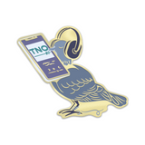 An enamel pin shaped like a blue bird wearing headphones, holding a cellphone that is playing TNO.