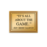 Gold metal rectangular pin that resembles a plaque that says, "IT'S ALL ABOUT THE GAME. ~SGT. ERNIE CALHOUN".