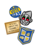 Blue metal circular pin with the words "VOtE FOR KI" with yellow stars. Black Metal pin of a grey robot smiling with red and green eyes. Gold metal rectangular pin that resembles a plaque that says, "IT'S ALL ABOUT THE GAME. ~SGT. ERNIE CALHOUN". And a silver metal pin in the shape of a shield to resemble the VGHS Crest with it's pixelated designs in each of the four corners. 