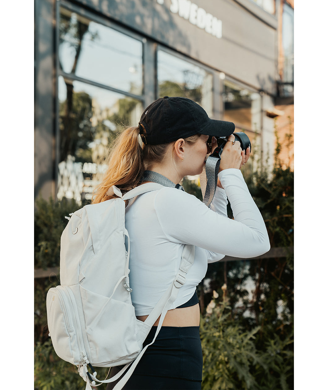 Lizzie Peirce wearing a hat, a backpack and holding a camera to her face.