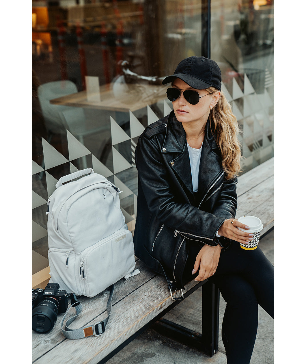 Lizzie Peirce wearing a hat and sunglasses with a camera and backpack next to her.
