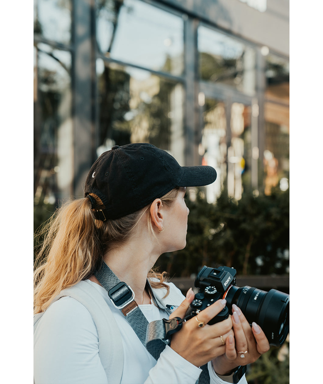 Lizzie Peirce wearing a hat, looking into the distance and holding a camera. The hat has a small white crescent embroidered on the back.