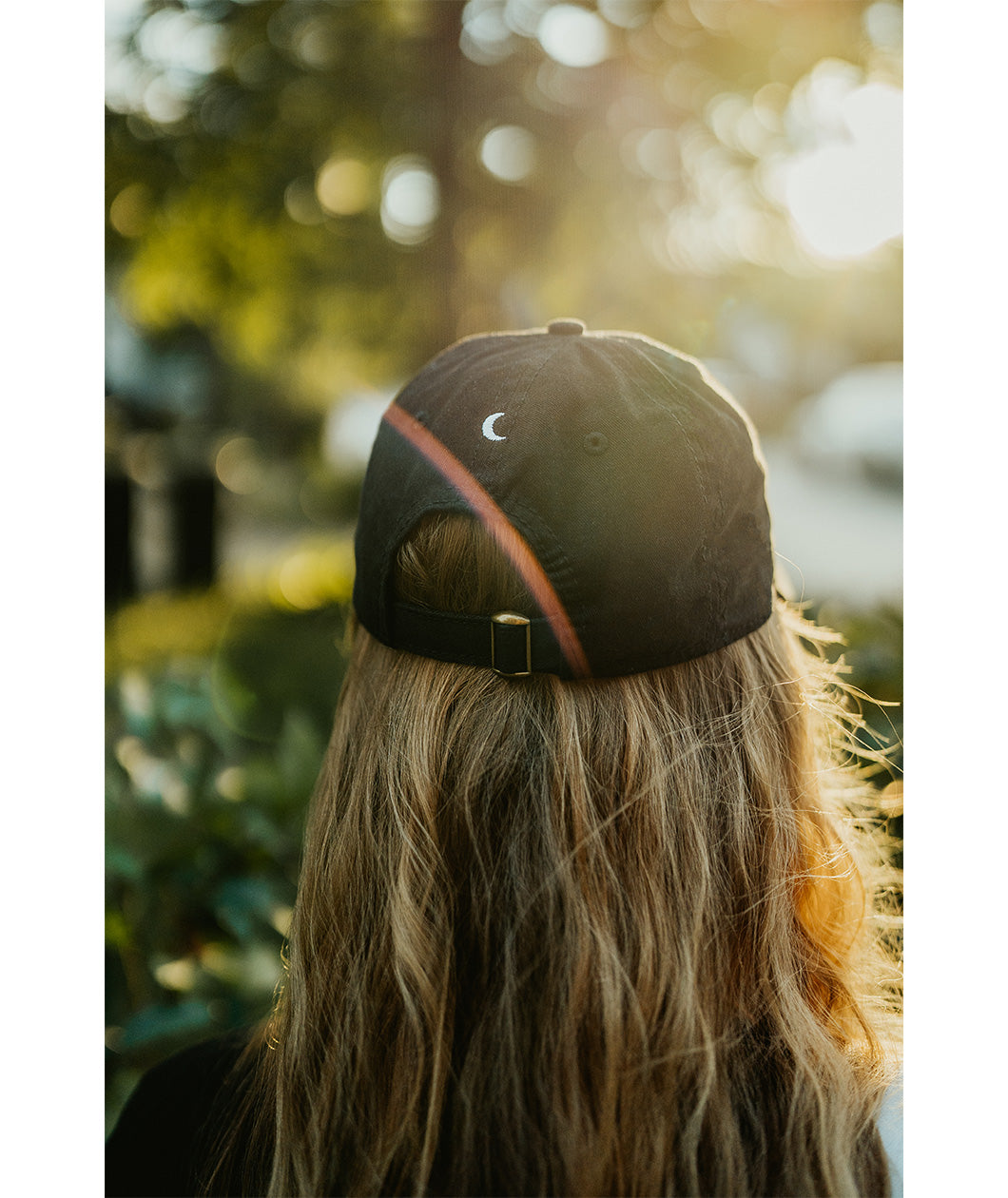 Lizzie Peirce wearing a hat, with her back to the camera. The hat has a small white crescent embroidered on the back.