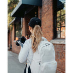 Lizzie Peirce wearing a hat, looking into the distance and holding a camera. The hat has a small white crescent embroidered on the back.