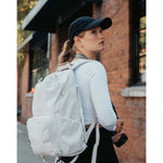 Lizzie Peirce wearing a hat, looking into the distance and holding a camera. The hat has a small white crescent embroidered on the back.
