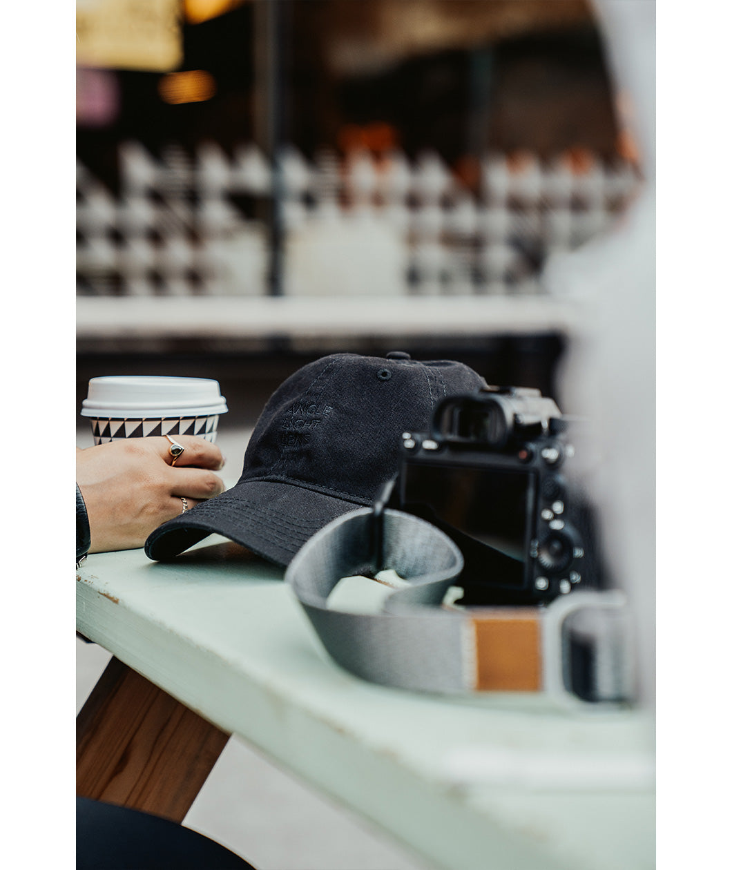A black hat embroidered with "Angle Light Lens" sits on a table with a camera next to it.