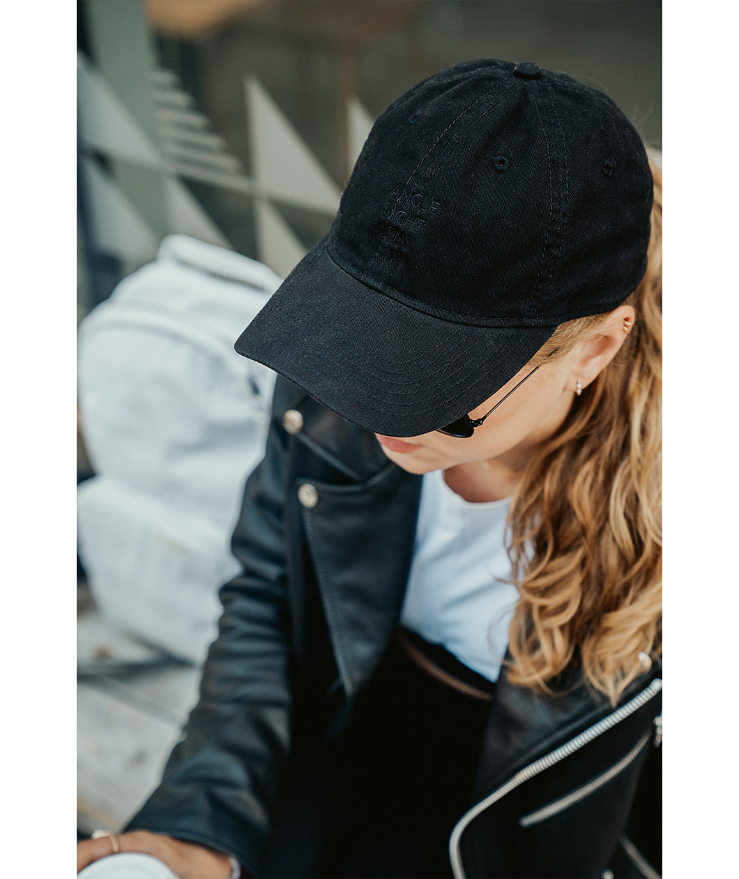 Lizzie Peirce wearing a hat with her head pointed down. The hat is black and is embroidered with "Angle Light Lens."