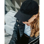 Lizzie Peirce wearing a hat with her head pointed down. The hat is black and is embroidered with "Angle Light Lens."