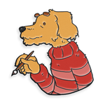 A pin shaped like the top half of a dog. The dog is a sandy color swearing a striped red sweater and holding a paintbrush. The painting dog pin from Mateusz Urbanowicz.