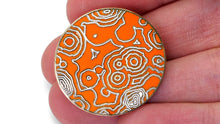 A NileRed circular orange pins showing abstract lines being held in someones fingertips.