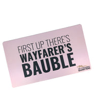 A pink rectangular playmat with curved edges. “First Up There’s Wayfarer’s Bauble” is in black sans serif font in varying weights in the center. “The Commander’s Quarter’s” is in the bottom right of the playmat with a signature above - from the Commander’s Quarters
