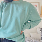 Mayuko Inoue modeling a mint green crewneck sweater with “code;” embroidered in the top right of the sweater in mint green - from Hello Mayuko