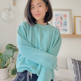 Mayuko Inoue modeling a mint green crewneck sweater with “code;” embroidered in the top right of the sweater in mint green - from Hello Mayuko