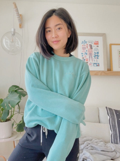 Mayuko Inoue modeling a mint green crewneck sweater with “code;” embroidered in the top right of the sweater in mint green - from Hello Mayuko