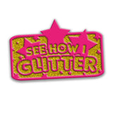 Rectangular pin with curves edges. Outline is in red with a gold glitter fill. “See how I glitter” is outlined in red with gold glitter fill. Red stars surround text in varying sizes with one in the center breaking the boundary of rectangle - from Lindsay Ellis