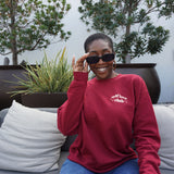 A woman modeling a red crewneck sweatshirt with “Self love” in white serif font outlined in orange arched above “club” in white serif font outline in orange. “Club” is surrounded by orange stars - from Sierra Schultzzie