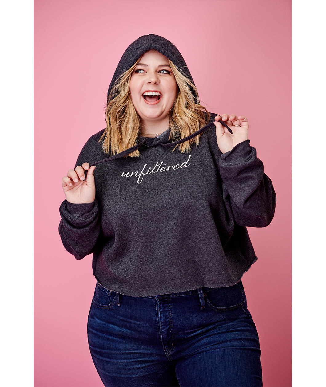 A woman modeling a dark gray crop top hoodie with “unfiltered” in white cursive font across the chest - from Sierra Schultzzie