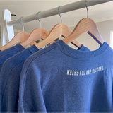 A set of blue crewnecks hanging on hangers with "Where all are welcome" written across the top of the backs. From Sierra Schultzzie.
