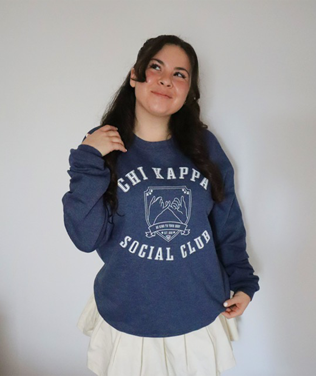 A person wearing an oversized blue crewneck that reads "Chi Kappa; Social Club" across the front with a picture of two pinkys intertwined. From Sierra Schultzzie.