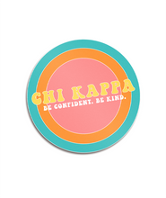 A circular sticker with a colorful, ringed background that says "Chi Kappa; Be confident. Be kind." From Sierra Schultzzie.
