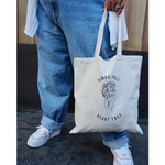 Close up of someone holding the canvas tote from Sierra Schultzzie with the words "Hands Full, Heart Full" printed in black as well as an outline of a hand holding flowers.