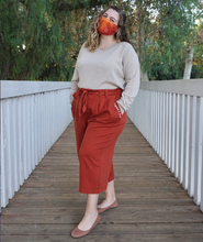 A woman modeling copper colored pants with a copper colored belt tied in a knot. “Confident & Kind” is in white curisve font along the lefthand pocket - from Sierra Schultzzie