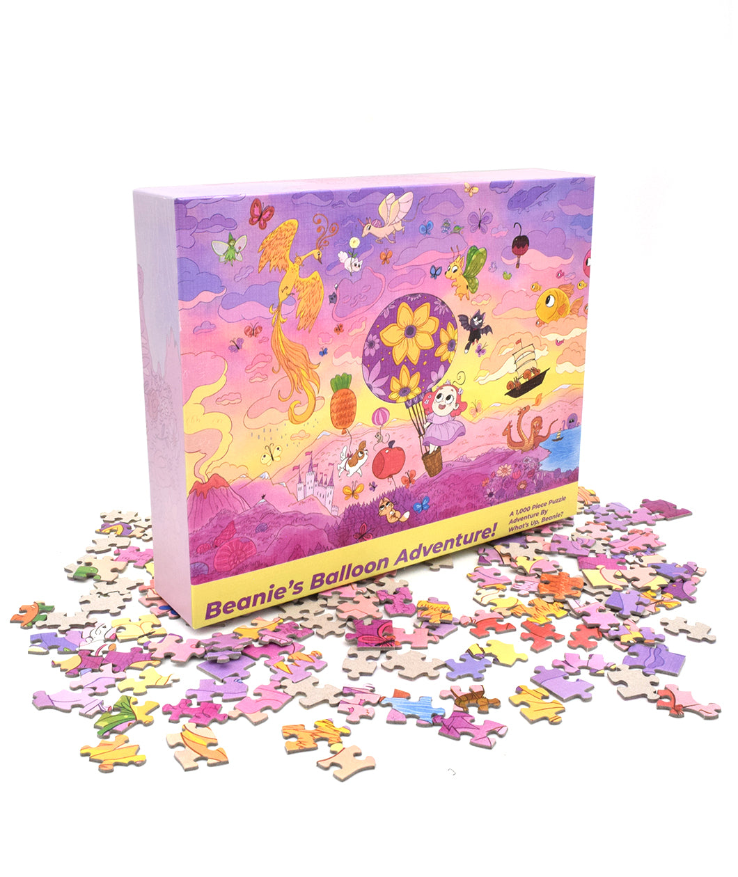 A rectangular puzzle box atop a pile of colorful puzzle pieces. The puzzle box has a pink and yellow sunset scheme and features a girl with pink hair in the basket of a purple hot air balloon decorated with flowers. The balloon floats amid a menagerie of whimsical objects in a sunset sky. Along the bottom of the box is the text 