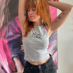 A photo of Catherine McCafferty posing, wearing a cropped gray tank top. The tank top reads "Pretty Gay" and has little star illustrations around it. From Pretty Gay.