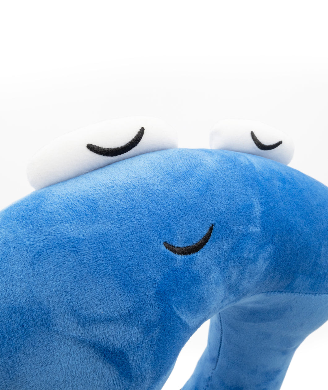 A closeup of a blue neck pillow in the shape of a pi character. The pillow is blue, and the pi character has a sleeping face. From 3Blue1Brown.