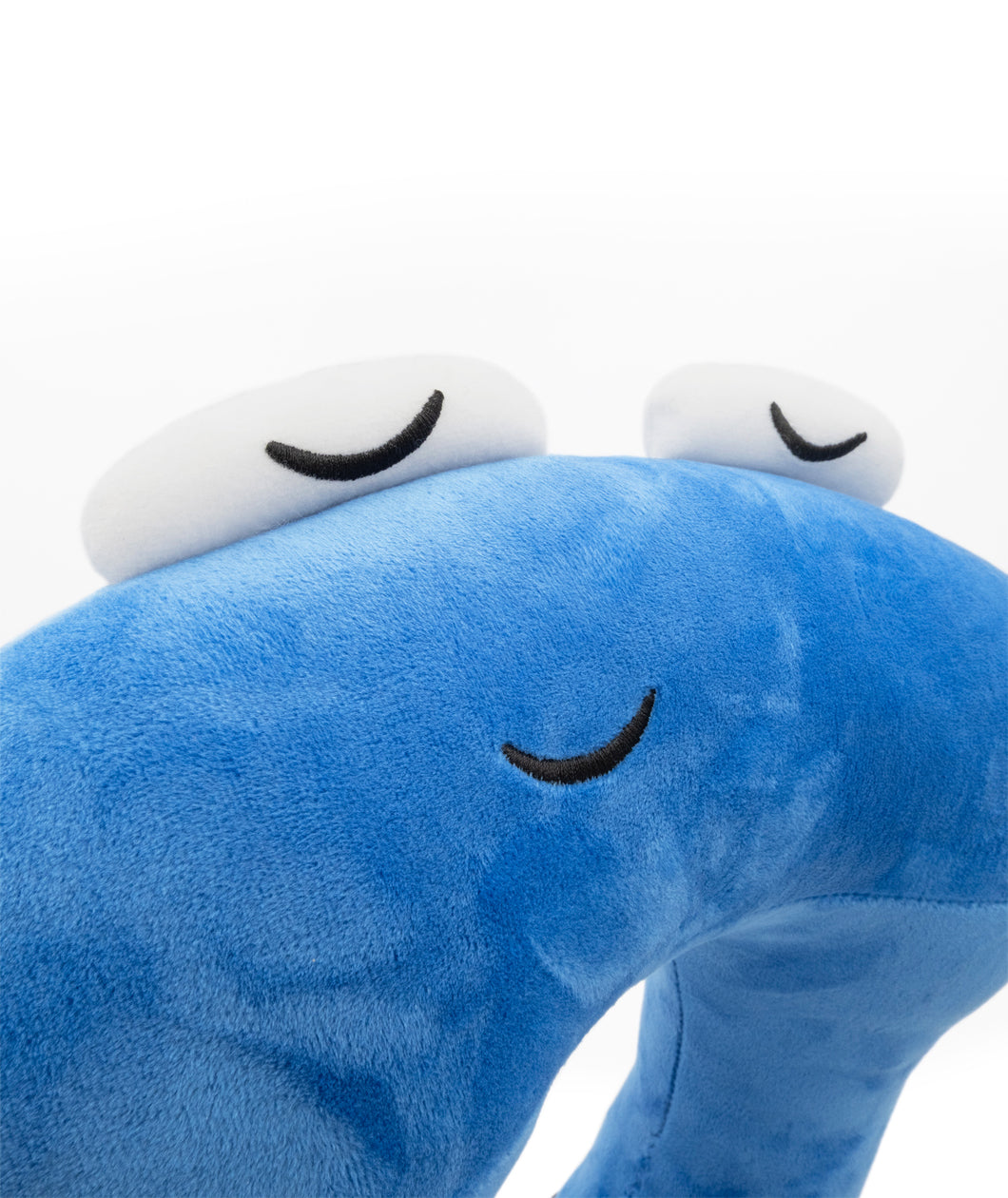 A closeup of a blue neck pillow in the shape of a pi character. The pillow is blue, and the pi character has a sleeping face. From 3Blue1Brown.
