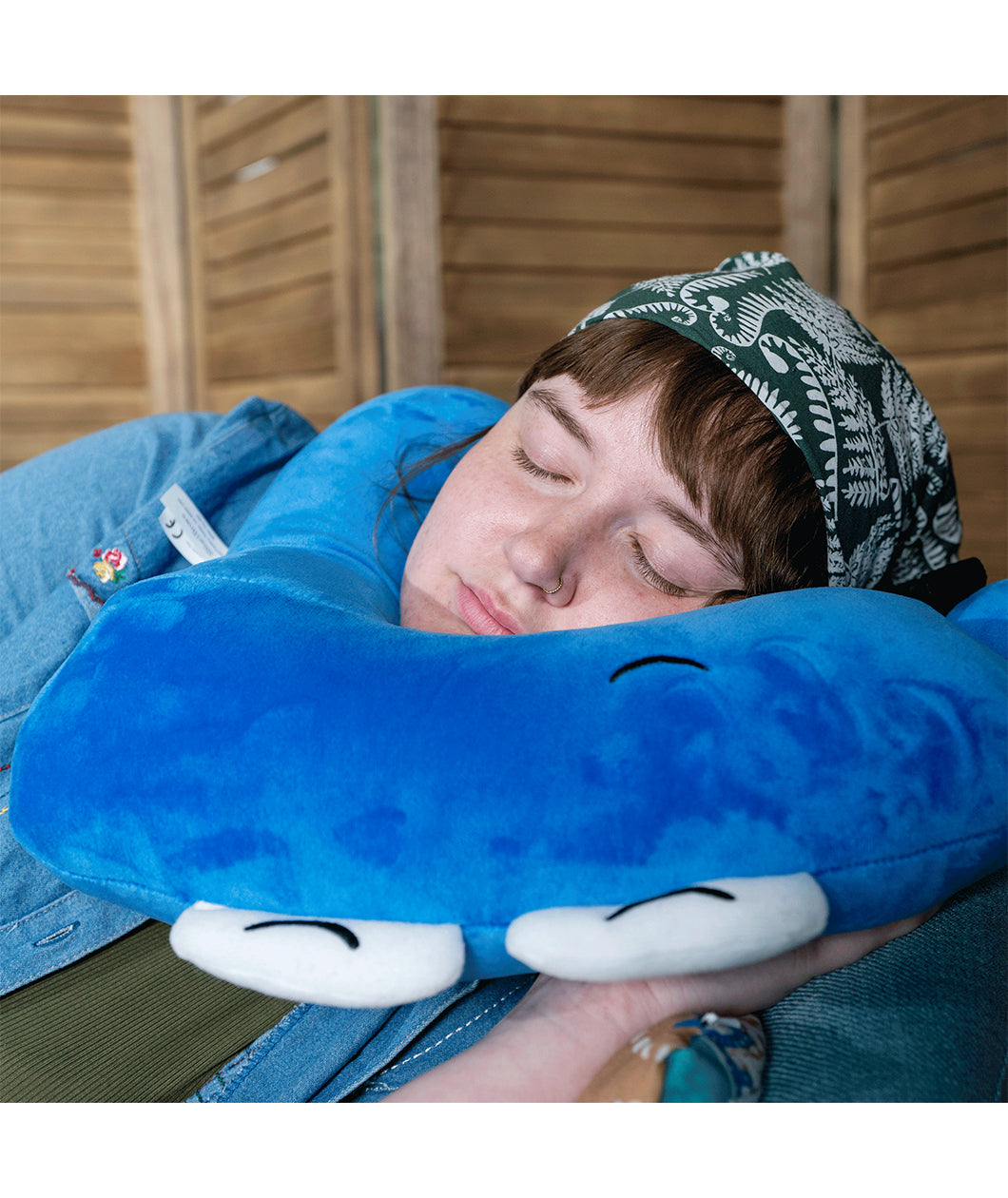 A person laying down and using a neck pillow to sleep. The person is using a neck pillow that is in the shape of a blue pi character. From 3Blue1Brown.