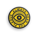 Yellow and black circular pin with an eye in the center and the phrase "Always read the plaque" surrounding it - by 99% Invisible