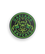 Green and black circular pin centering a cat with the phrase "Oakland Raycats" around it - by 99% Invisible