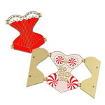 Gold hard enamel pin shaped like a corset filled with red enamel and a white enamel top edge to look like lace with gold detailing. The pin is split down the middle with golden hinges on each of the four corners to show it can open. The pin is then shown open below to reveal the words "HO HO HO" in the center with candy can patterned padding on each hip and a candy cane candy bra with white enamel lace. Small magnets are on the back of the two open front flaps.