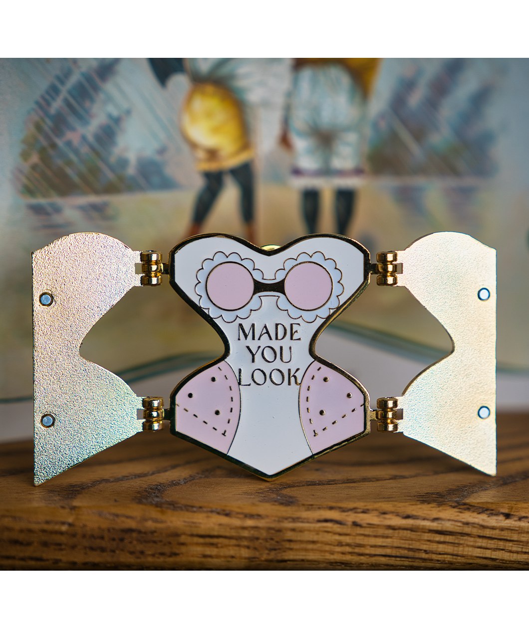 Gold hard enamel pin has either side opened to reveal the words "MADE YOU LOOK" in the center with slightly darker pink padding on each hip and a pink bra with white enamel lace. Small magnets are on the back of the two open front flaps.