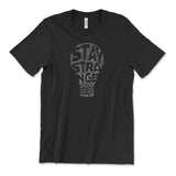 A black t-shirt with a lightbulb in the center made up of small, white text with negative space that reads "Stay Strange". From Atypical Artists.