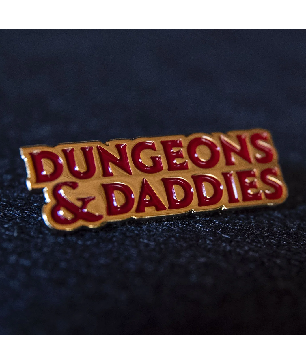 Gold plated enamel pin of Dungeons & Daddies logo in red enamel.