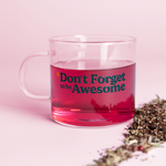 Clear glass mug with the words "*Don't Forget to be Awesome" on it in teal text. Sitting next to pile of loose leaf tea, mug is filled with magenta tea.