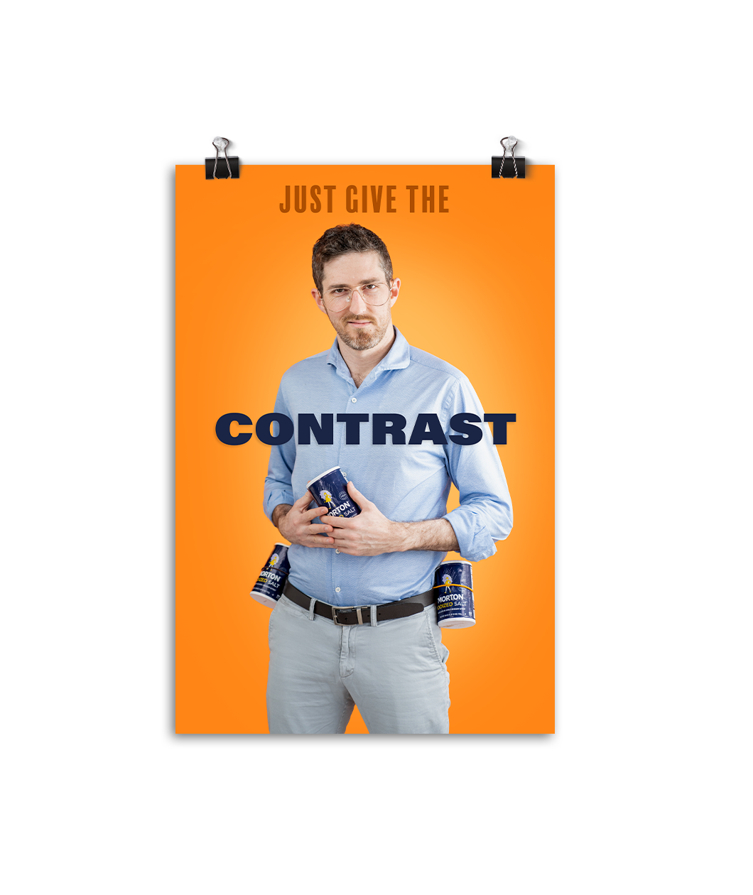 Poster of a man holding the Mornton's salt container. Text above him says, " JUST GIVE THE" and text overlayed says, "CONTRAST". Poster background is orange.