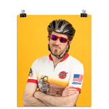 Photo of a man crossing his arms in a zip up bike shirt, bike helmet, and sun glasses smirking at the camera. On a yellow background.