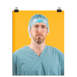 Photo of a man in seafoam colored scrubs and aviator shaped glasses wearing a seafoam hair net looking stone faced at the viewer. On a yellow background.