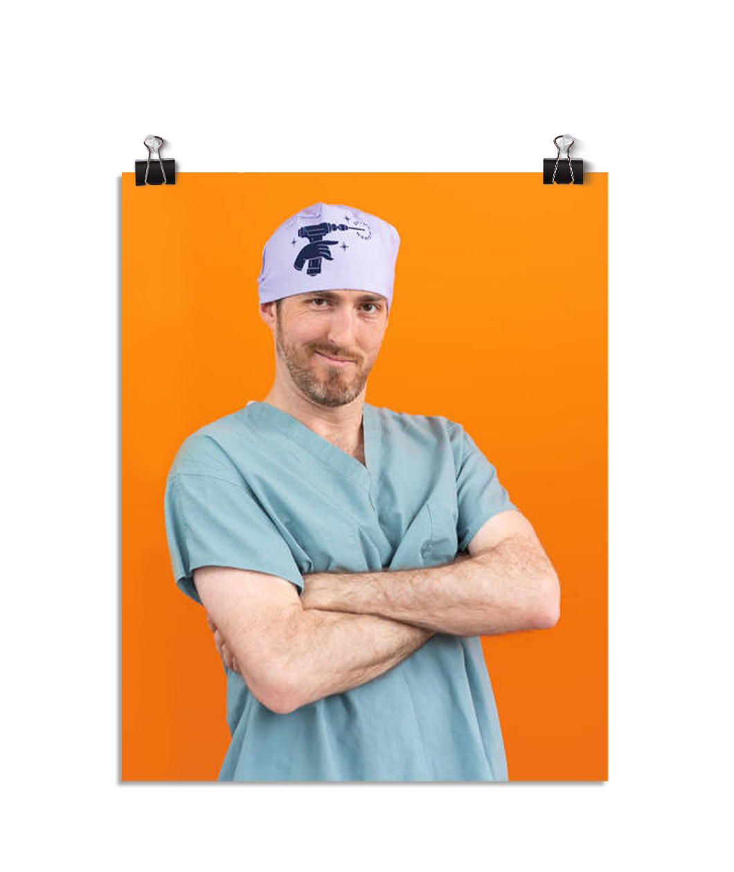 Photo of a man in seafoam colored scrubs and a light purple head wrap with an embroidered hand holding a drill. His arms are crossed as he leans to his right and smirks at the viewer. On an orange colored background.